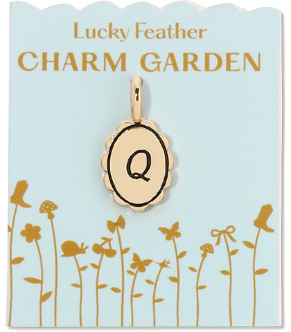 A gold-colored charm with the letter 'Q' hangs from a blue card that reads 'Lucky Feather CHARM GARDEN' and features illustrations of flora and fauna.