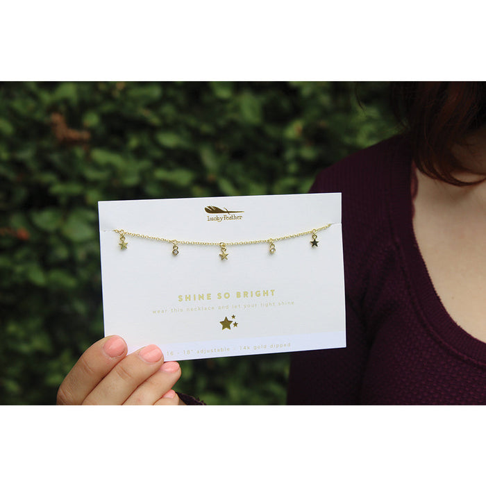 A hand holds a product card displaying a gold-colored necklace with star charms.