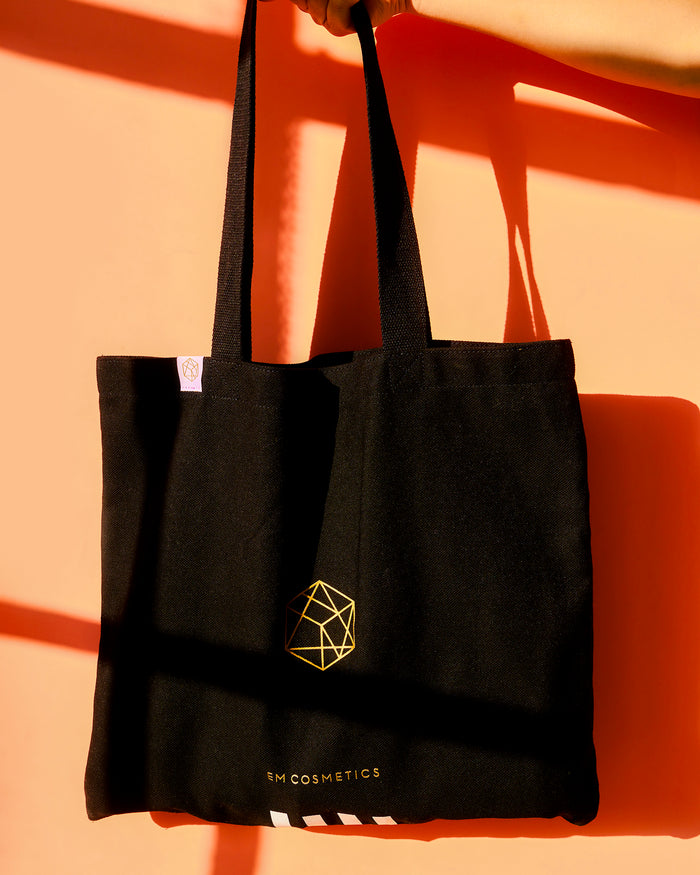 A stylish, minimalist white canvas tote bag with the black EM Cosmetics logo, perfect for carrying daily beauty essentials.