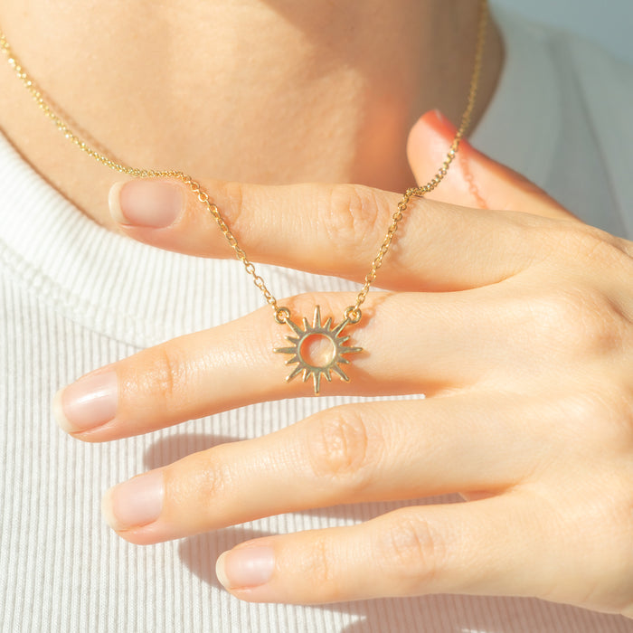 A person's hand holds a gold sunburst pendant necklace.