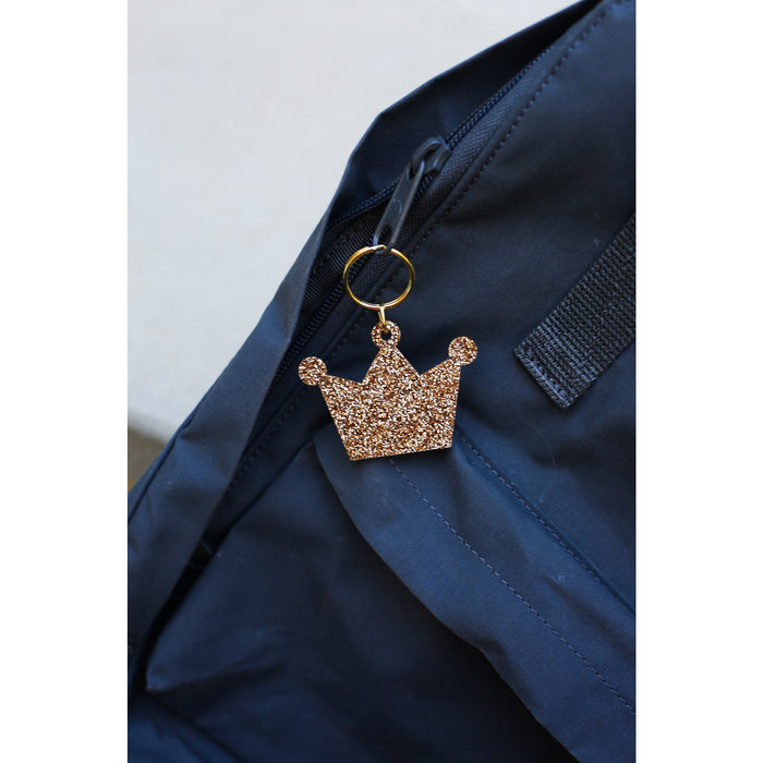 A glittery gold crown keychain hangs from the zipper of a navy blue bag.