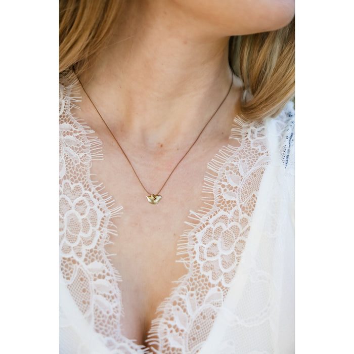 A person wearing a white lace top and a gold bird necklace with a brown cord.