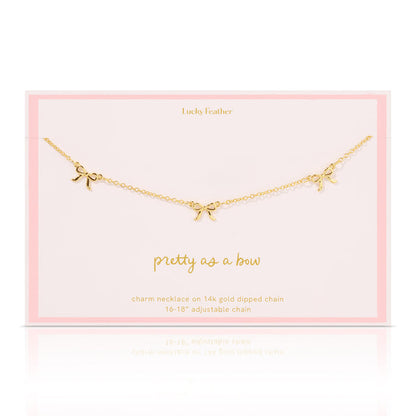 A gold charm necklace with three bows displayed on a pink card that says 'Lucky Feather'.