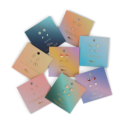Several sets of stud earrings on colorful, gradient cards are arranged in a circle on a white surface.