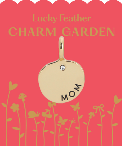 A gold 'mom' charm with a gemstone on a pink card featuring flowers.