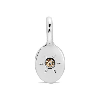 A silver charm with a central amber-colored gem and rays.