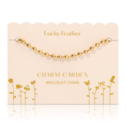 A gold bead bracelet chain on a decorative 'Lucky Feather Charm Garden' display card.