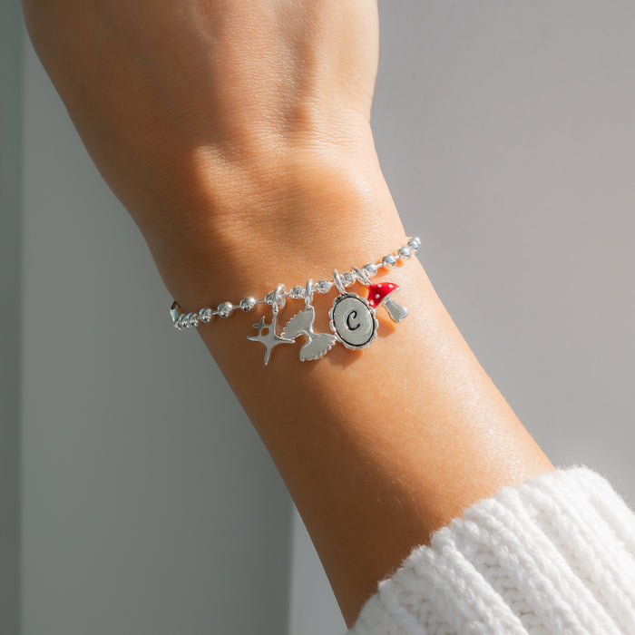 A silver charm bracelet with a letter 'C' and a mushroom charm is on a wrist.