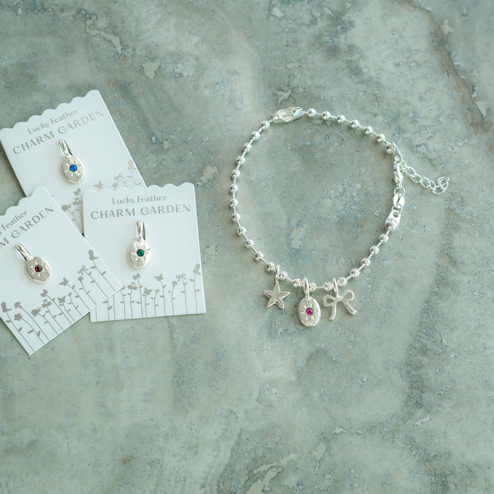 A silver charm bracelet and charm pendants on cards are arranged on a textured gray surface.