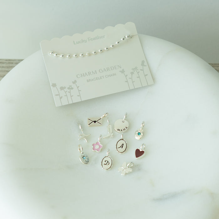A 'Lucky Feather' bracelet chain and various charms arranged on a marble surface.