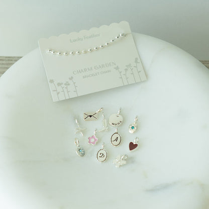 A 'Lucky Feather' bracelet chain and various charms arranged on a marble surface.