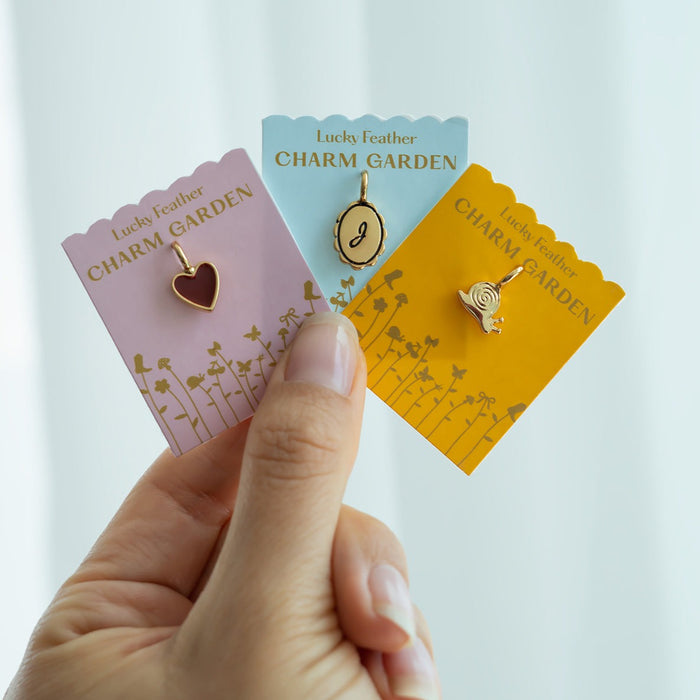 Hand holding three 'Lucky Feather Charm Garden' cards with a heart, letter, and snail charm.
