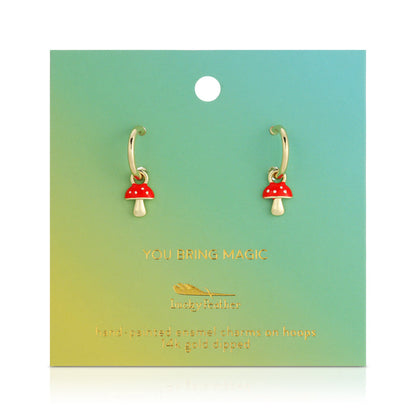 Gold hoop earrings with red and white mushroom charms are displayed on a green and yellow gradient card.