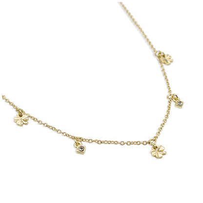 A delicate gold necklace with clover and gem charms is displayed on a white background.