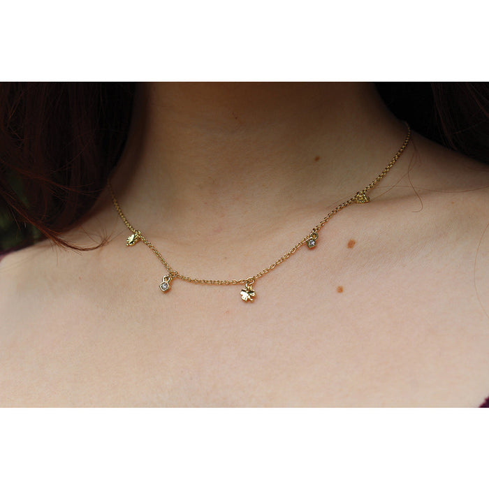 A person wears a gold necklace with clover and diamond-shaped pendants.