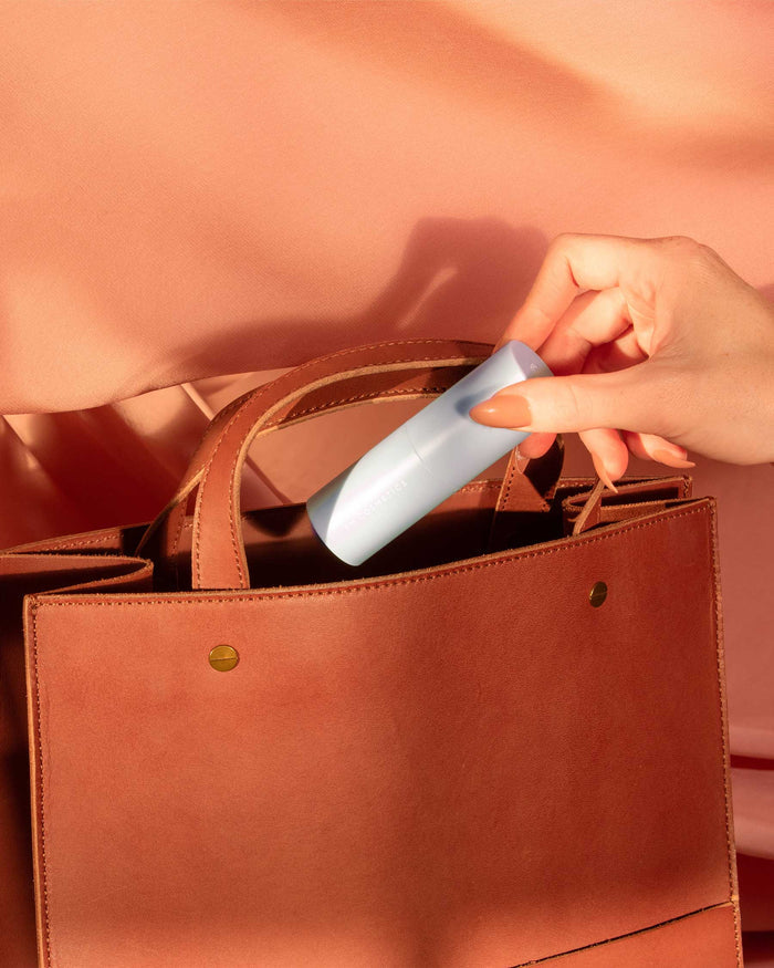 Lifestyle shot of the EM Cosmetics Face Cuddle Moisture Balm in a purse, emphasizing its travel-friendly design.