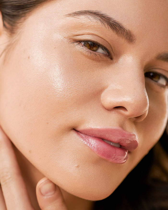Model with medium skin applies EM Cosmetics Face Cuddle Moisture Balm to cheekbones for a fresh, dewy, glass-skin glow.