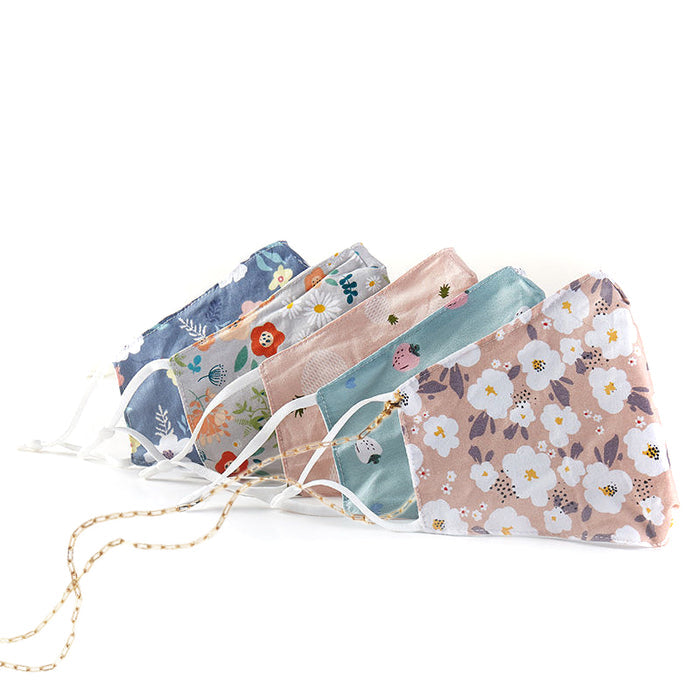 Five cloth face masks with floral designs line up with ear straps and a gold chain.