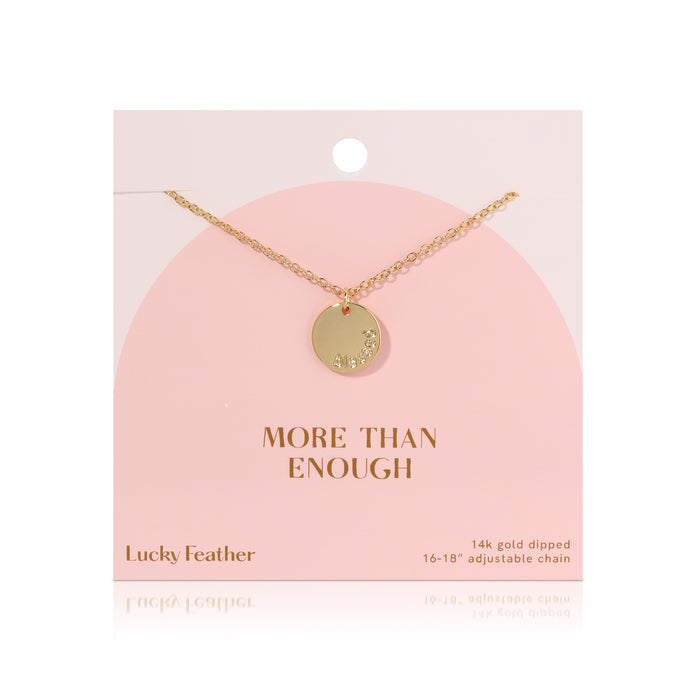 A 14k gold dipped necklace with a round pendant hangs against a pink card with 'MORE THAN ENOUGH' printed on it.