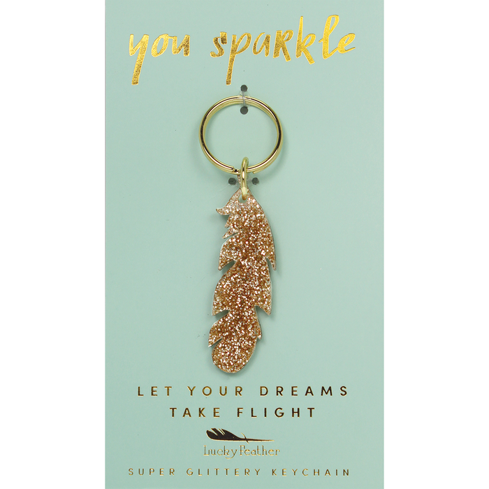 A gold glitter feather keychain hangs on a light blue display card.