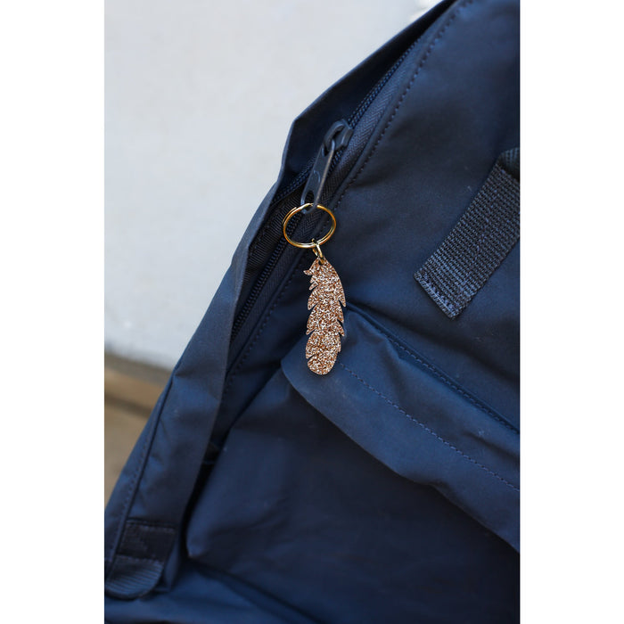 Two smiling women hold up a 'Lucky Feather' brand sparkly feather keychain against a blue background.