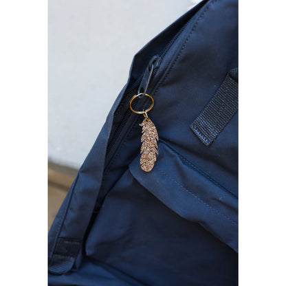 Two smiling women hold up a 'Lucky Feather' brand sparkly feather keychain against a blue background.