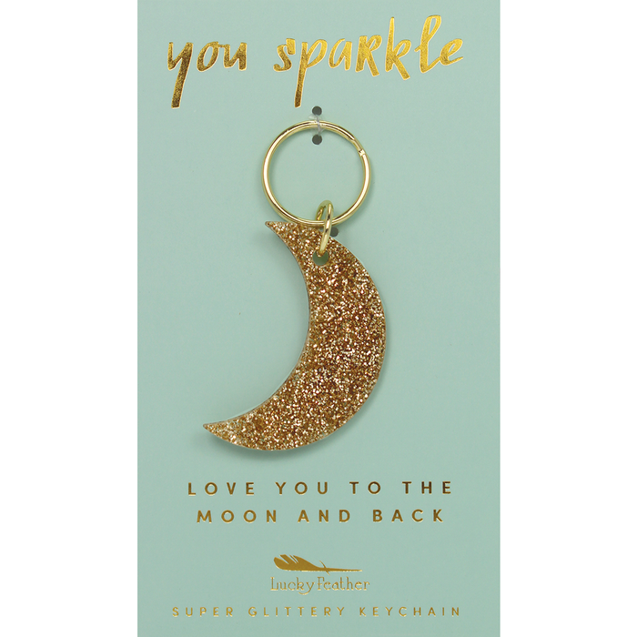 A crescent moon keychain with gold glitter is displayed on a light green card with gold lettering.