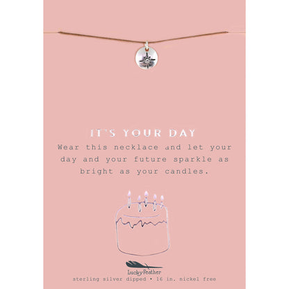 A necklace with a round pendant on a pink card that says 'It's Your Day'.