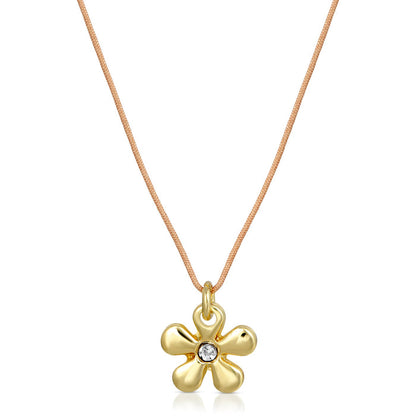 A necklace with a gold flower pendant and a small, clear gemstone on a tan cord.