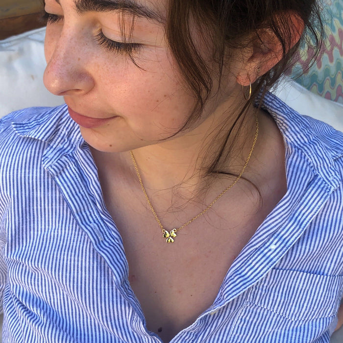 A person with eyes closed wearing a blue and white striped shirt and a gold butterfly necklace.