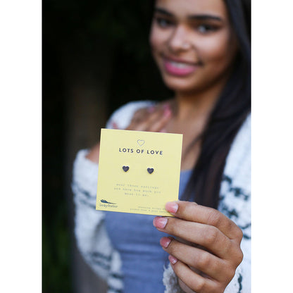 A person holds up a yellow card displaying heart-shaped earrings, with the words 'LOTS OF LOVE' printed on it.