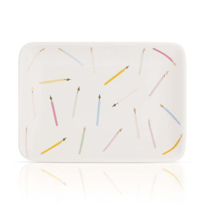Rectangular white dish decorated with candle illustrations, seen at an angle with a reflective surface below.