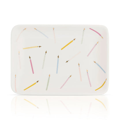 Rectangular white dish decorated with candle illustrations, seen at an angle with a reflective surface below.