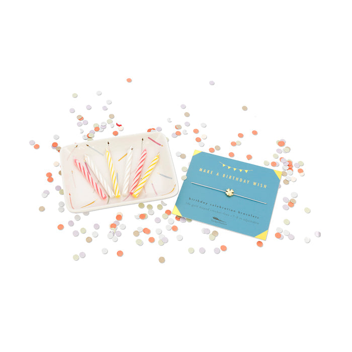 A dish of birthday candles and a 'Make A Birthday Wish' bracelet card are surrounded by colorful confetti.