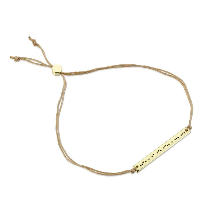 A tan cord bracelet with a gold-colored rectangular charm engraved with dots and dashes.