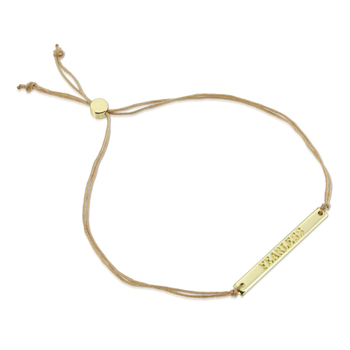 A bracelet with a gold-colored bar that says 'FEARLESS' on a beige cord.