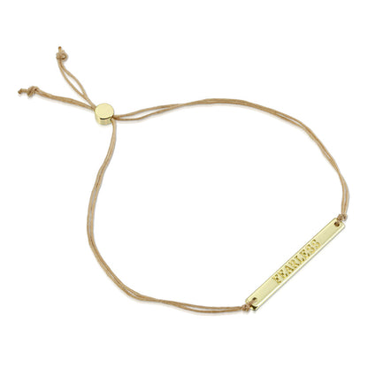 A bracelet with a gold-colored bar that says 'FEARLESS' on a beige cord.