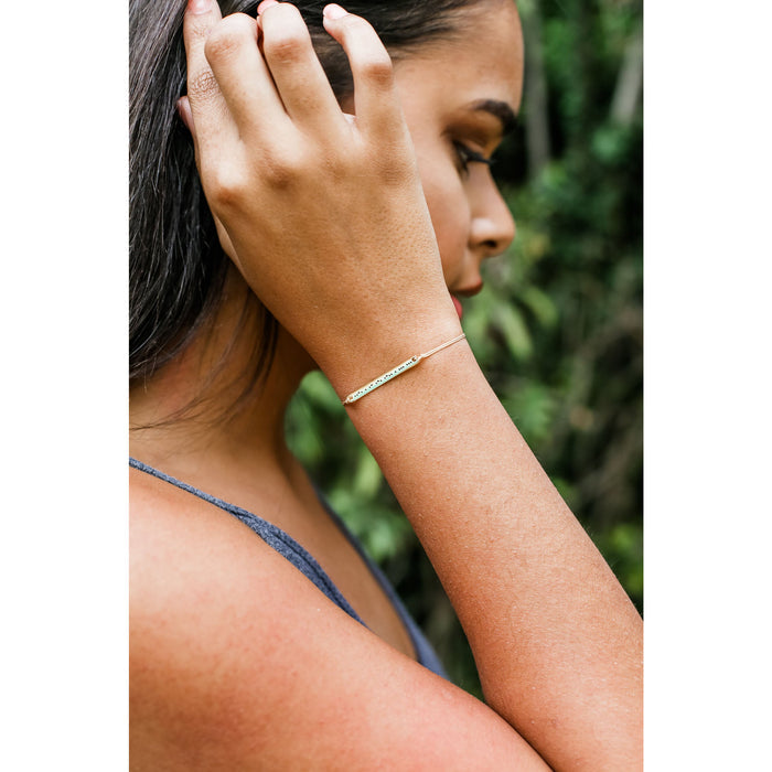 A person with dark hair and a blue tank top wearing a bracelet.