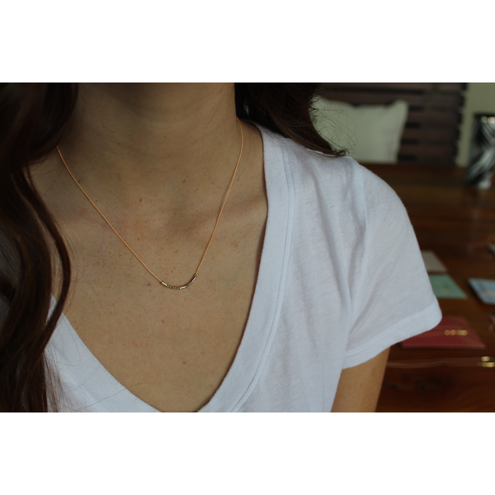 A woman in a white t-shirt is wearing a delicate necklace with a bar pendant made of beads.