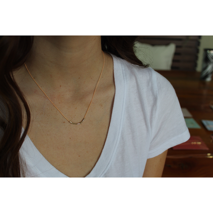 A woman in a white t-shirt is wearing a delicate necklace with a bar pendant made of beads.