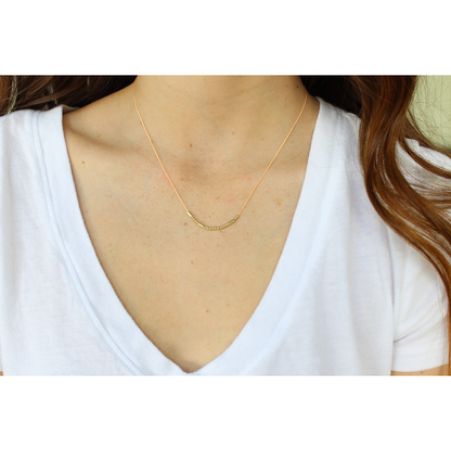 A person wearing a white v-neck shirt and a gold beaded necklace.