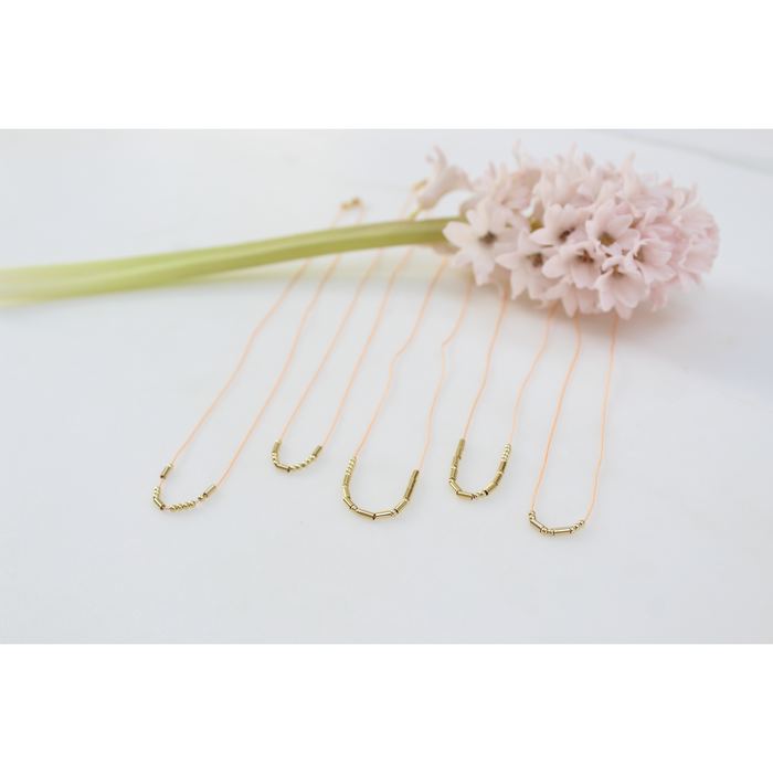 Five beaded necklaces and a pink hyacinth flower rest on a white surface.
