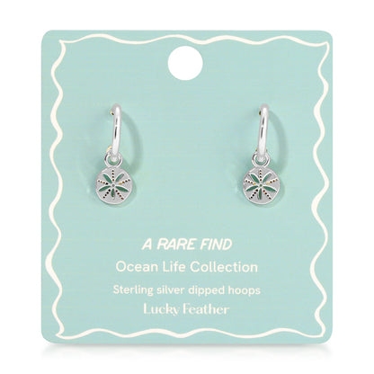 Two silver hoop earrings with sand dollar charms are displayed on a blue-green product card.