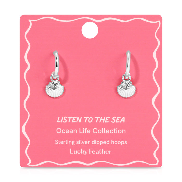 Two sterling silver hoop earrings with seashell charms are displayed on a pink card.