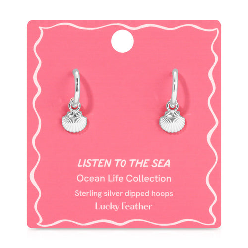 Two sterling silver hoop earrings with seashell charms are displayed on a pink card.