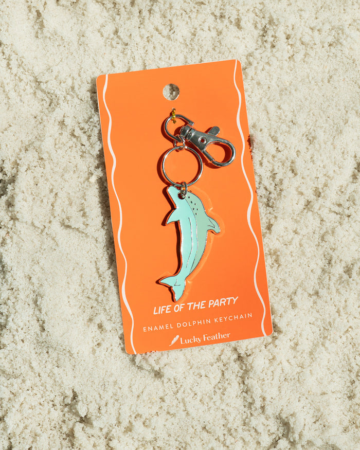 A dolphin keychain on an orange tag rests on sand.