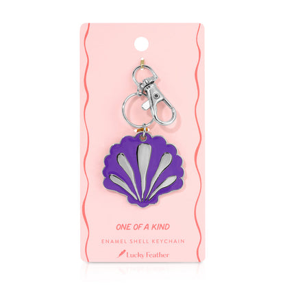 A purple enamel shell keychain with a silver clasp on a pink display card.