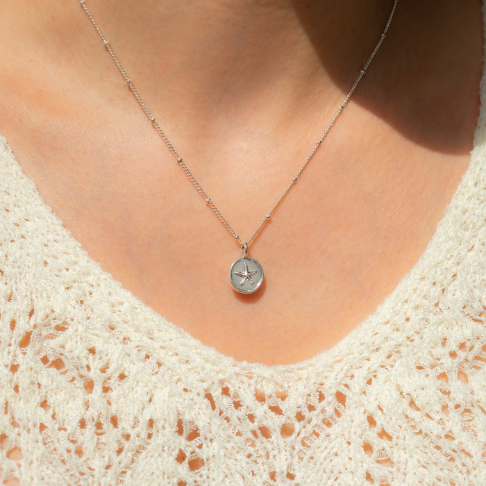 A person wearing a silver necklace with a round pendant featuring a starfish.