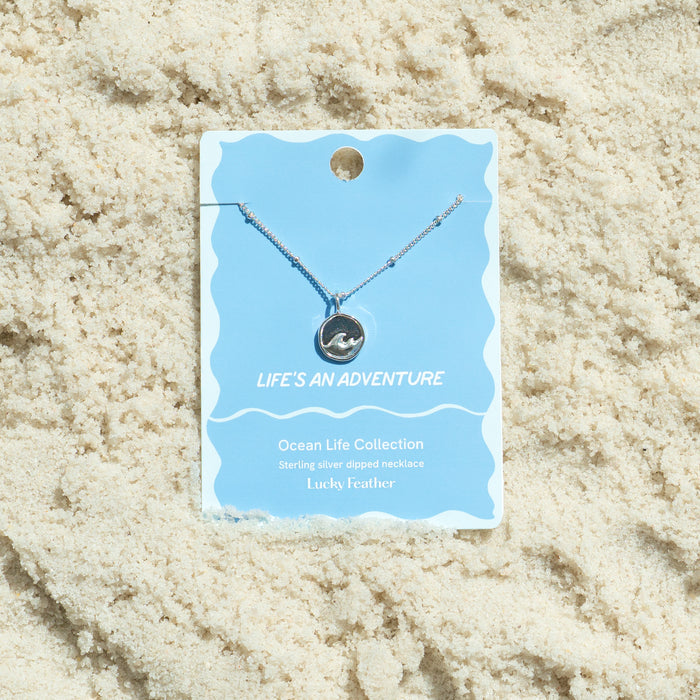 A necklace on a product card is displayed on sand.
