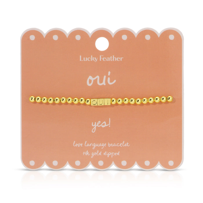 The image shows a gold-colored beaded bracelet with the word 'OUI' spelled out in letter beads, displayed on a peach-colored product card.
